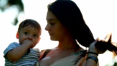 Mom holding baby son in outdoor park with lens-flare