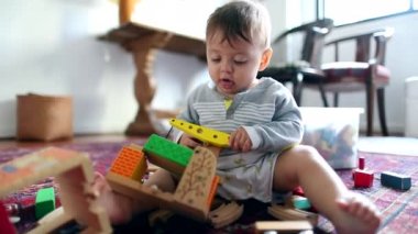Adorable cute baby toddler playing with toys indoors at home seated