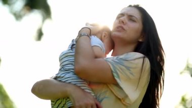 Authentic real life mother consoling baby son in outdoor nature with lens-flare