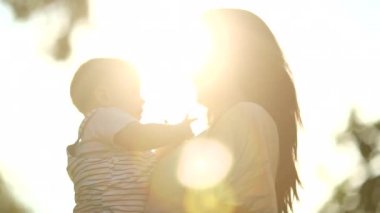 Authentic mother holding happy baby infant son in outdoor nature with lens-flare sunshine