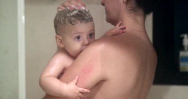 Mother and baby in shower together. Mom cleaning toddler hair with shampoo