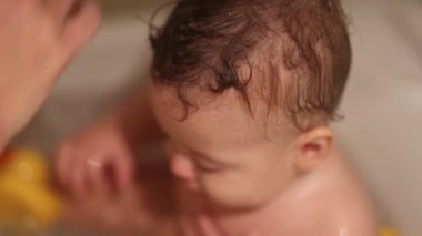 Showering baby with water inside bathtub, bathing infant boy