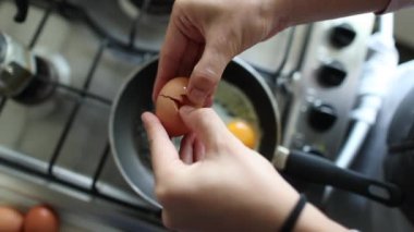 Close-up of hands breaking egg, frying on pan