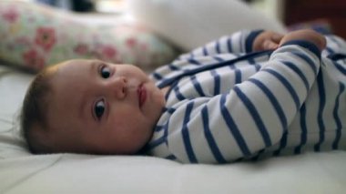 Beautiful handsome baby toddler laid in bed looking to camera being cute