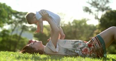 Mother holding baby infant in the air laid on grass outside during sunset