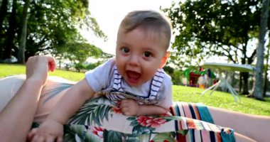 Happy baby looking to camera wanting to touch lens during sunset with lens-flare in outdoor park during sunset