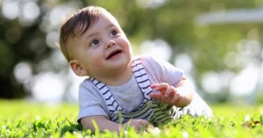Happy baby toddler laid on grass outside in nature smiling