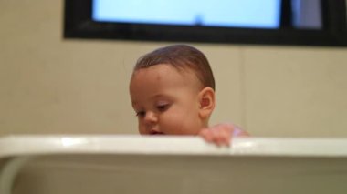 Bathing infant baby boy inside bathtub looking to camera curious