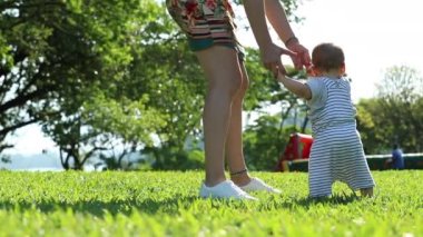 Child baby learning to walk. Mother helping infant toddler first steps