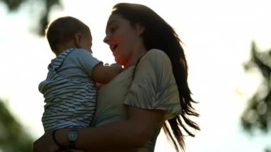 Authentic mom holding baby infant son child outdoors in sunset lens-flare
