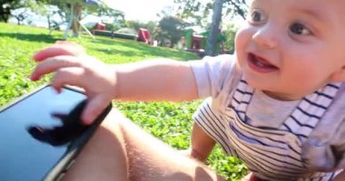 Baby toddler reaching to get smartphone on father lap outside in nature