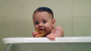 Baby playing with toy teething inside bathtub. Bathing happy infant toddler