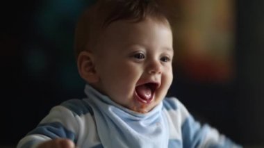 Happy baby holding and teething with infant spoon. Toddler face portrait closeup