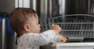 Adorable sweet baby toddler seated next to dishwasher touching equipment wanting to explore
