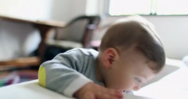Cute upset baby learning to stand by holding to sofa, infant touching ear