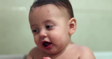 Cute baby inside bathtub holding yellow duck in mouth smiling and happy