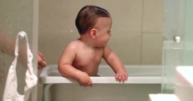 Cute baby toddler holding into bathtub side