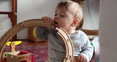 Baby playing with toys, infant putting road wooden toy in mouth