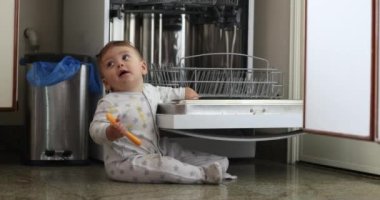 Adorable sweet baby toddler seated next to dishwasher touching equipment wanting to explore