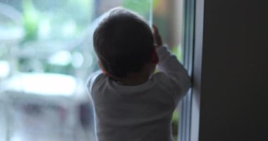 Baby by window looking out, wanting to go outside, infant on tiptoes