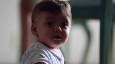 Cute baby boy turning head towards camera smiling feeling happy. Adorable toddler infant male turns head towards viewer