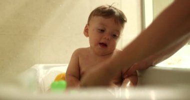 Bathing baby infant inside bathtub. Parent washing and cleaning toddler