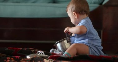 Baby playing with kitchen utensils holding pots and pans at home, creative curious toddler infant