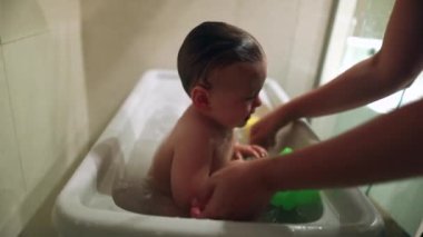 Cute baby inside bathtub. Parent bathing washing and cleaning toddler infant. Authentic family routine