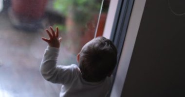 Baby infant wanting to go outside, toddler standing by window looking out, child effort to slide window