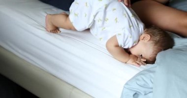 Baby learning to get out of bed with help of parent. Infant toddler descending bed
