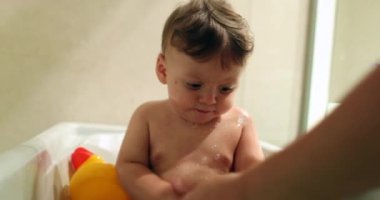 Parent washing baby infant inside bathtub splashing water into belly