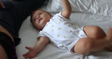 Baby infant with mother in bed together. Real life parent relationship interaction with toddler lying in bed