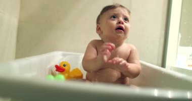 Cute baby infant inside bathtub, mother washing toddler son