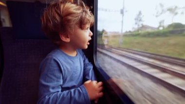 Child travels by train looking outside through window glass