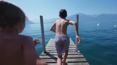 Çocuklar iskelede koşuyor ve yaz günü süper yavaş çekimde göle atlıyorlar.