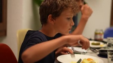 Yemek masasında yemek yiyen genç bir çocuk.