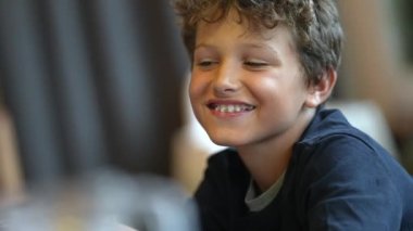 Genç bir çocuk kamera önünde el sallayarak selam veriyor.