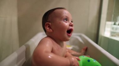 Smiling happy baby toddler inside bathtub playing with toy teething. Bathing infant playing
