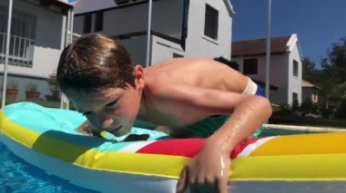 Yüzme havuzunda şişme yatakta vücudu dengeleyen çocuk