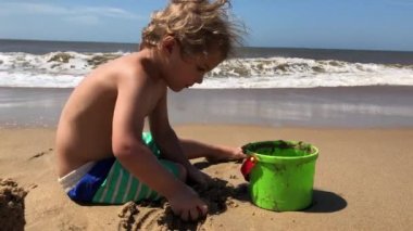 Infant playing with sand toys at the beach. Water waves disrupting child play