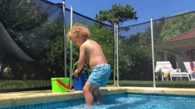 Toddler baby boy playing at swimming pool gathering water with bucket