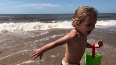 Infant toddler running at the beach with bucket filled with water playing