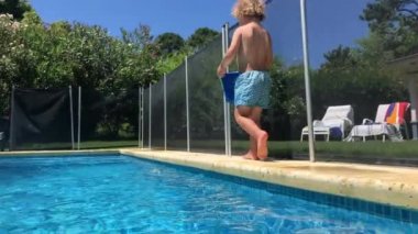 Toddler baby boy walking by poolside holding bucket