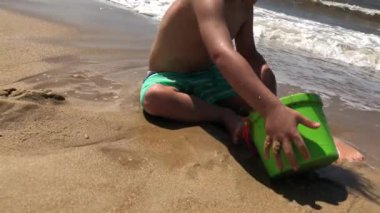 Küçük çocuk plaja kova fırlatıyor.