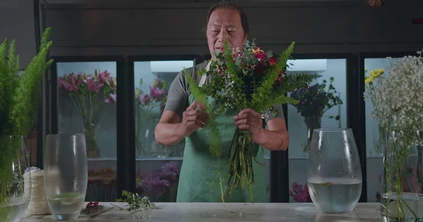 An Asian American florist preparing bouquet of flowers for online delivery. Portrait of an artisan male florist creating artistic arrangement for client at flower shop