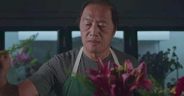 An Asian American florist preparing bouquet of flowers for online delivery. Portrait of an artisan male florist creating artistic arrangement for client at flower shop