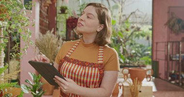 Female florist smiling at camera inside flower shop with arms crossed. Portrait of a young woman worker at small business store