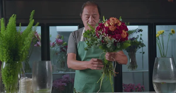 An Asian American florist preparing bouquet of flowers for online delivery. Portrait of an artisan male florist creating artistic arrangement for client at flower shop