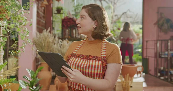 Female florist smiling at camera inside flower shop with arms crossed. Portrait of a young woman worker at small business store