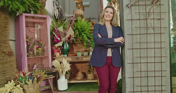 Portrait of female business owner of local flower shop standing in storefront smiling at camera with arms crossed. Happy entrepreneur of local small business flower store